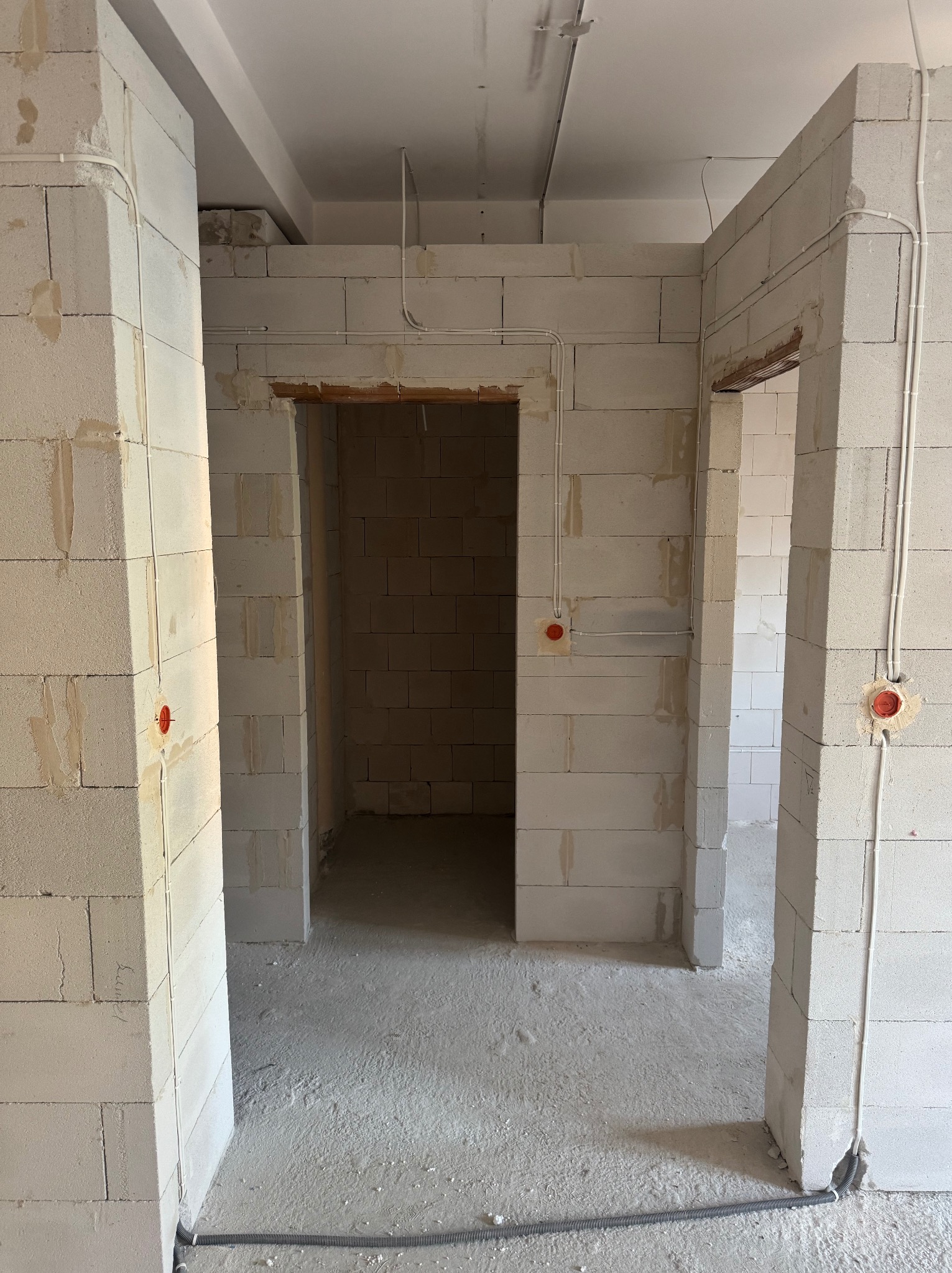 Surowy stan wnętrza z białych bloczków, widoczne kable elektryczne w peszlach i puszki instalacyjne. Wnętrze w trakcie prac wykończeniowych, brak tynków.