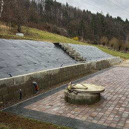 Sekwoja Garden - Przygotowany teren pod trawnik z rolki, widoczne schody i studzienka. Częściowo ułożona kostka brukowa. Na górze skarpy czarna mata, zabezpieczenie przed osuwaniem.