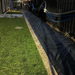 Sekwoja Garden - Układanie trawy z rolki w ogrodzie: widoczna świeżo ułożona darń, czarna mata szkółkarska i rury doprowadzające wodę wzdłuż ogrodzenia.