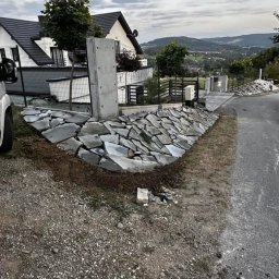 Sekwoja Garden - Skarpa z kamienia naturalnego ułożona wzdłuż drogi, z betonowym słupkiem. W tle dom z ogrodem i widok na góry. Efektowna aranżacja przestrzeni.