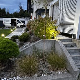 Sekwoja Garden - Ogród z niską roślinnością ozdobną, kamieniami i betonowym obrzeżem, z oświetlonymi ścieżkami i nowoczesnym domem z panelami słonecznymi w tle.