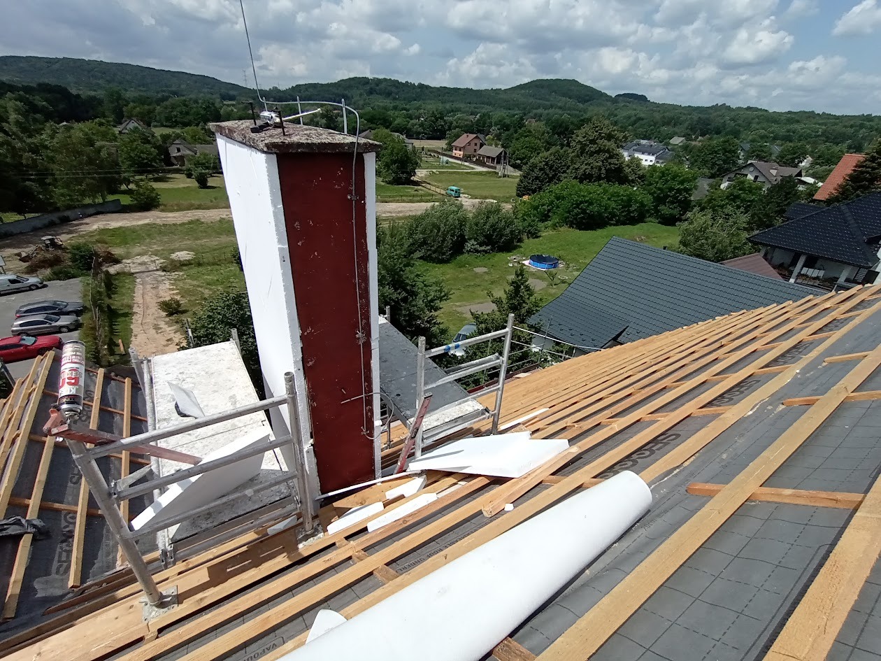 Szkielet dachu z kominem w trakcie prac izolacyjnych w Skawinie. Widoczne drewniane elementy konstrukcyjne i materiały izolacyjne.