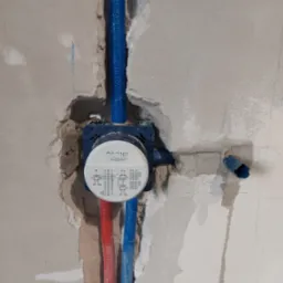 Instalacja podtynkowa Grohe w surowej ścianie: niebieskie i czerwone rury doprowadzające wodę, widoczne oznaczenia ciepłej i zimnej wody, przygotowanie do montażu armatury.