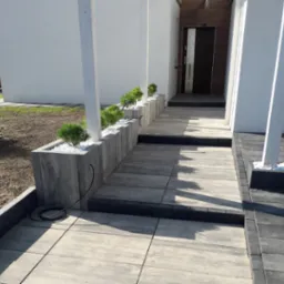 Nowoczesne podejście do domu z kostki brukowej w odcieniach szarości, z elementami dekoracyjnymi w postaci roślin i białych kamieni. Minimalistyczny design.