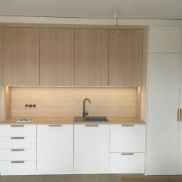 DARCO-USŁUGI MONTAŻOWE ZABIELSKI DARIUSZ - Jasna kuchnia na wymiar z drewnianymi akcentami: białe fronty, blat i szafki górne w odcieniu drewna, minimalistyczny zlew i bateria. Widoczne gniazdka i niedokończone oświetlenie.