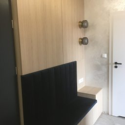 DARCO-USŁUGI MONTAŻOWE ZABIELSKI DARIUSZ - Jasna szafa wnękowa z siedziskiem obitym granatowym materiałem. Dwa szklane kinkiety na ścianie. Minimalistyczny design, jasne drewno, gładkie fronty.