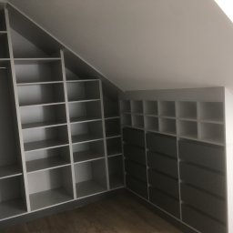 DARCO-USŁUGI MONTAŻOWE ZABIELSKI DARIUSZ - Szara szafa wnękowa z licznymi półkami i szufladami, dopasowana do skosu dachu. Widoczne drewniane panele podłogowe.