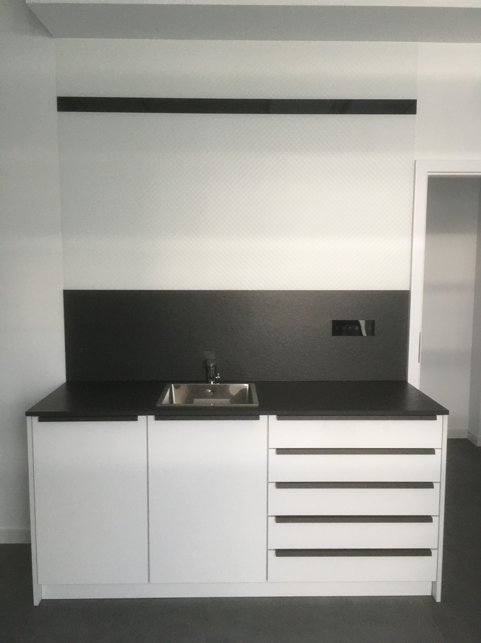 Nowoczesna zabudowa kuchenna z białymi szafkami, czarnym blatem i zlewozmywakiem. Minimalistyczny design, ciemne uchwyty i backsplash.