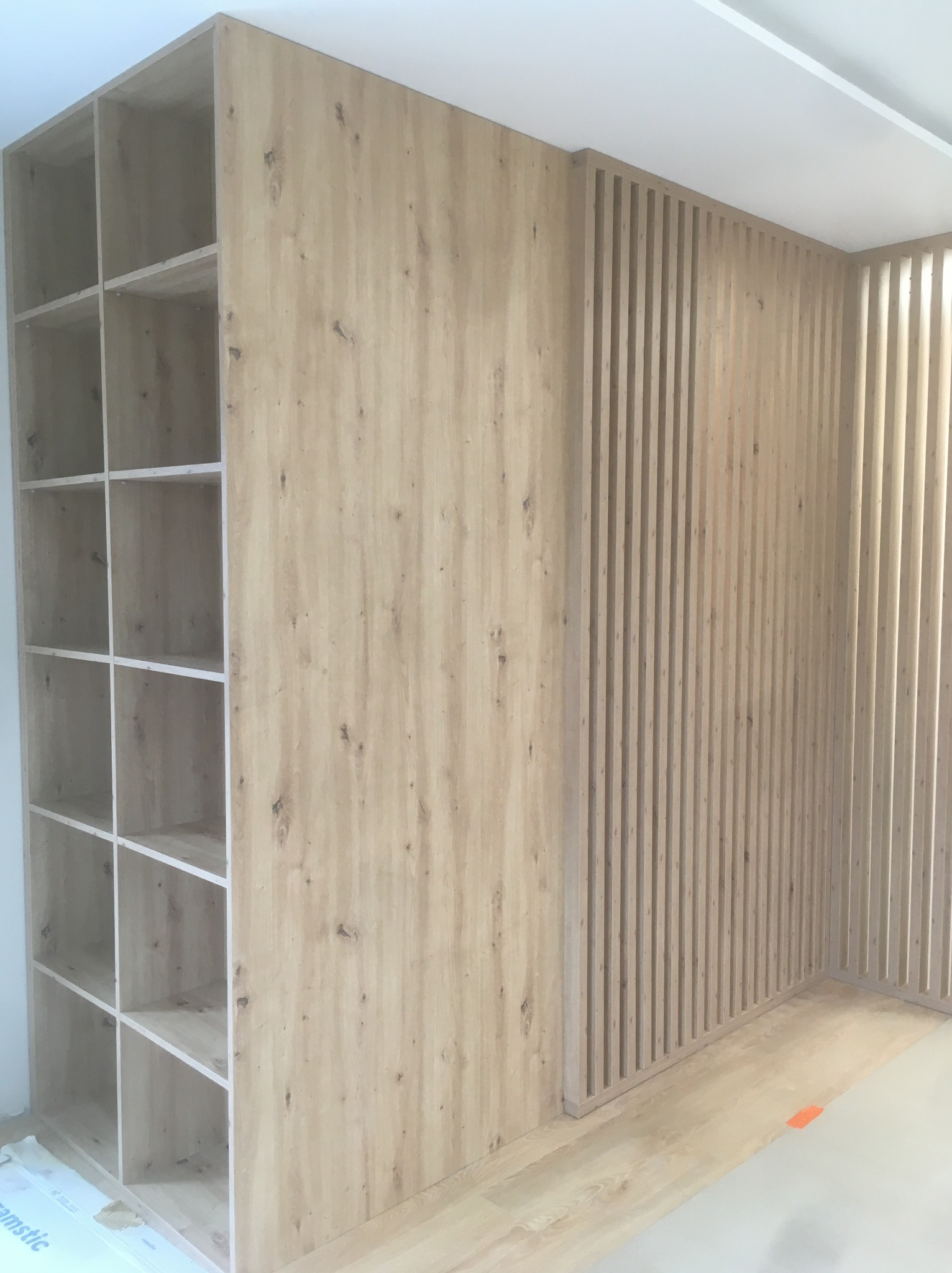 Drewniana szafa wnękowa z półkami i lamelami w odcieniach beżu, dopasowana do wnętrza. Nowoczesny design i funkcjonalność.