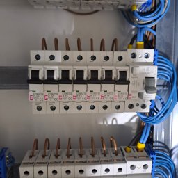 Instalacje Elektryczne Karol Banachowski - Szczegółowe ujęcie tablicy rozdzielczej z zainstalowanymi bezpiecznikami ETI i niebieskimi przewodami. Widoczne oznaczenia C10 i B16 na poszczególnych elementach.