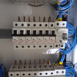 Szczegółowe ujęcie tablicy rozdzielczej z zainstalowanymi bezpiecznikami ETI i niebieskimi przewodami. Widoczne oznaczenia C10 i B16 na poszczególnych elementach.