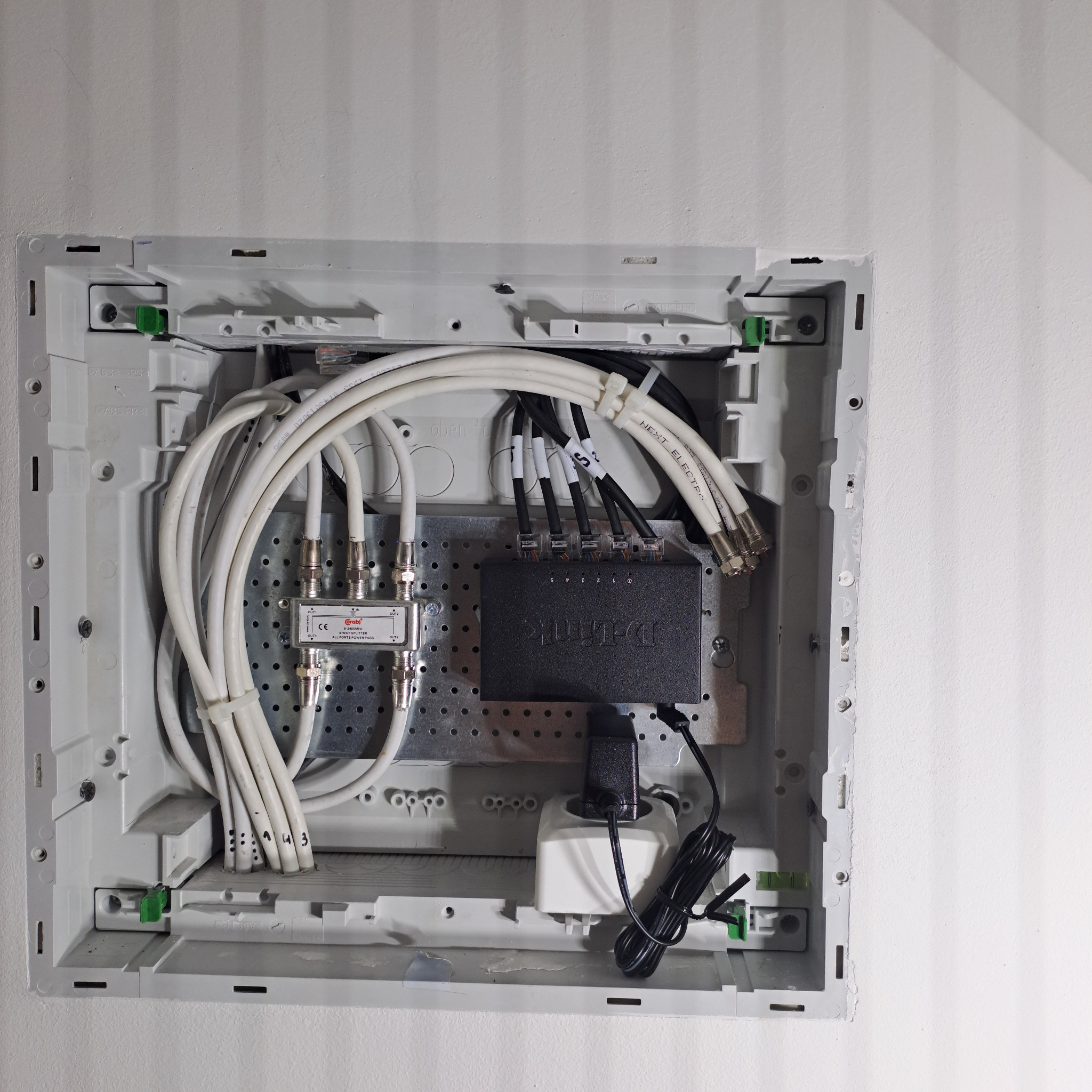 Rozdzielnica z kablami koncentrycznymi i rozgałęźnikiem, zamontowana na białej ścianie. Widoczne oznaczenia kabli i elementy złączne.