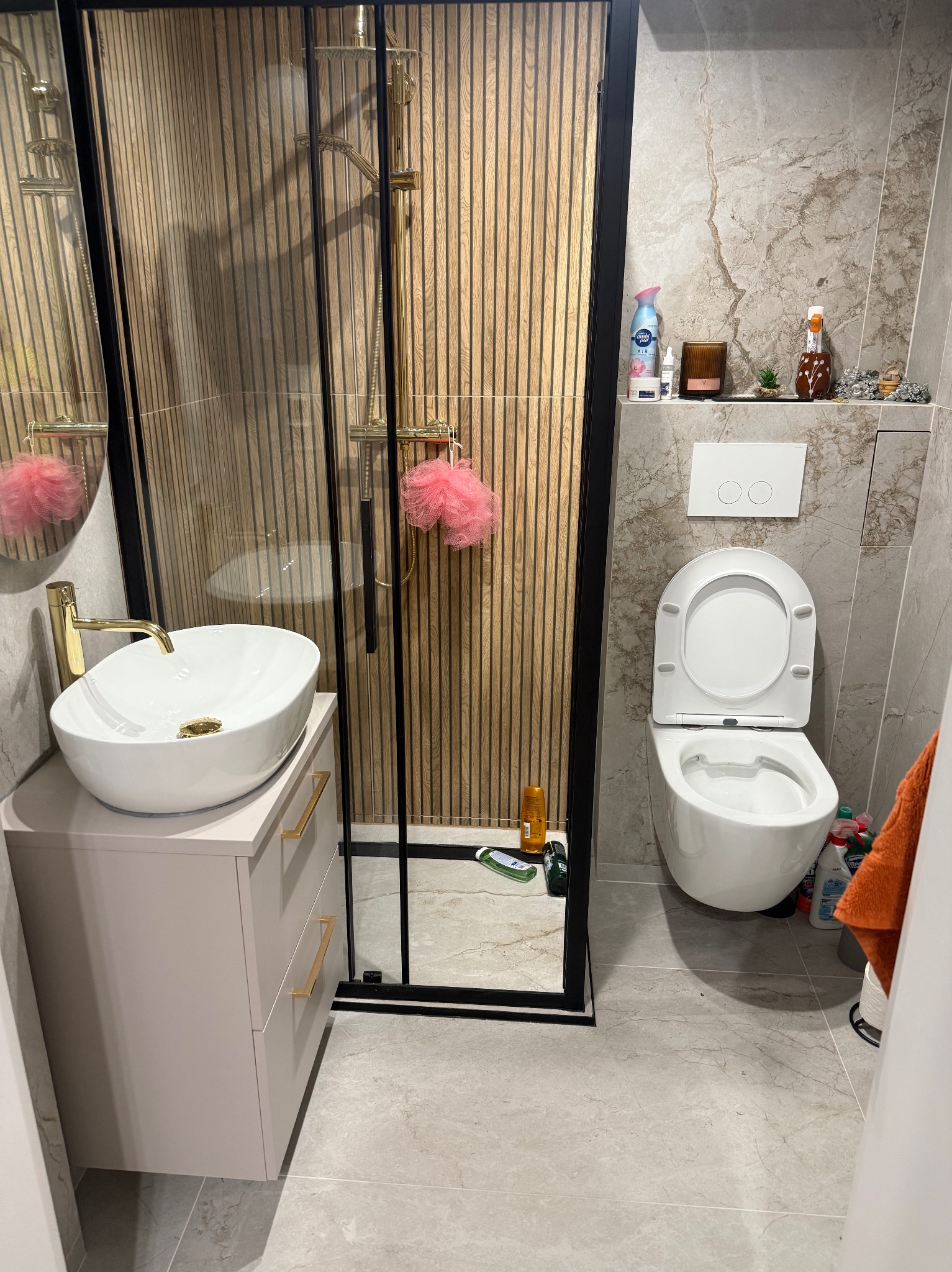 Nowoczesna łazienka z kabiną prysznicową typu walk-in, umywalką nablatową na szafce i toaletą. Ściany wyłożone płytkami imitującymi marmur, drewniane panele w kabinie.