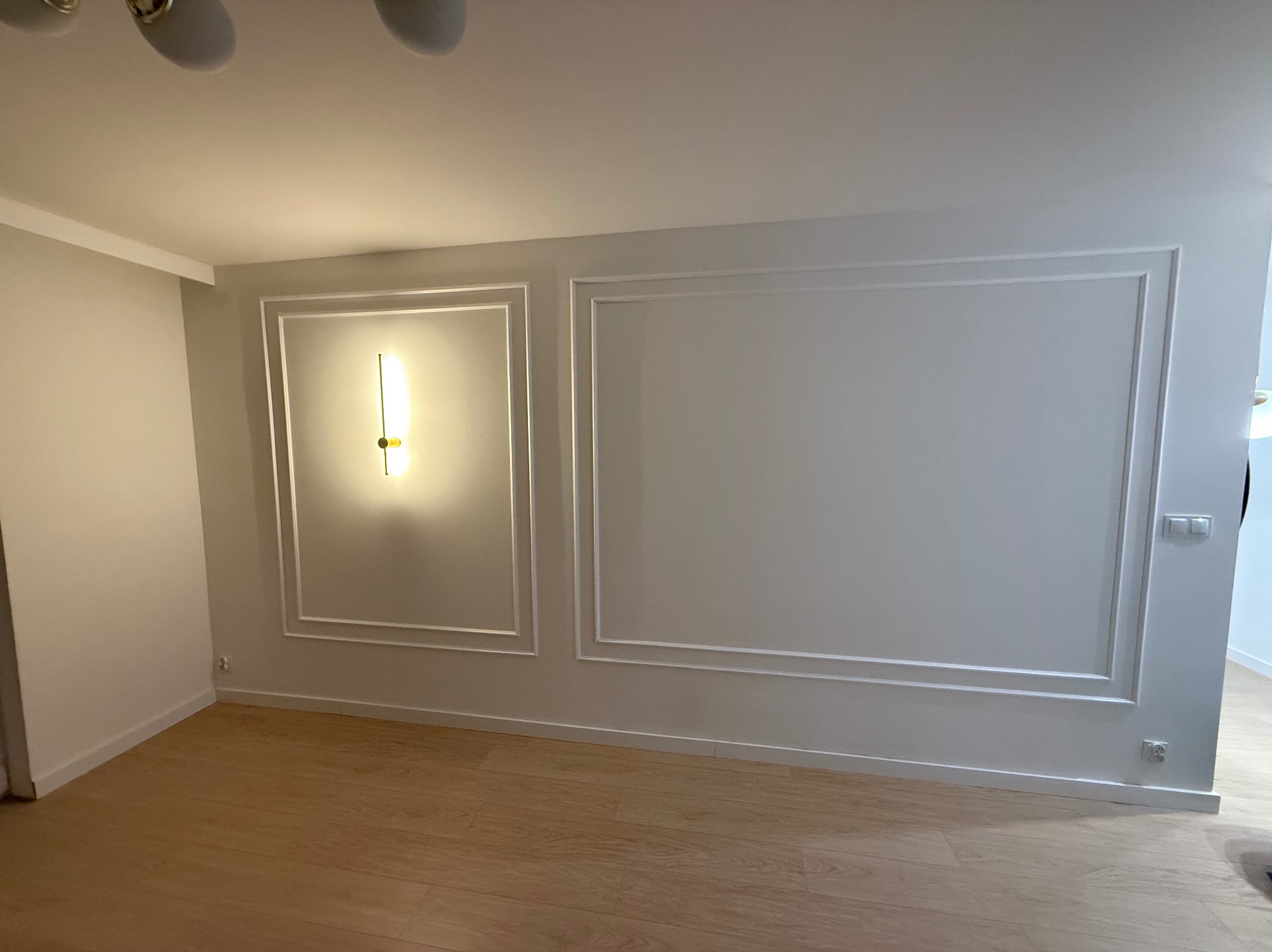 Białe ściany z dekoracyjnymi listwami i oświetleniem punktowym w pustym pokoju z drewnianą podłogą. Minimalistyczny design wnętrza.
