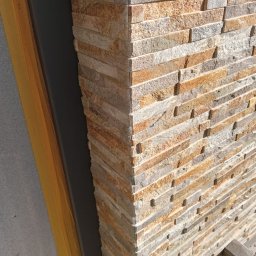 GALBUD SYLWIA GALOR - Wykończony narożnik ściany z dekoracyjnej, warstwowej okładziny kamiennej w odcieniach beżu i szarości. Widoczne detale faktury kamienia i precyzja ułożenia.