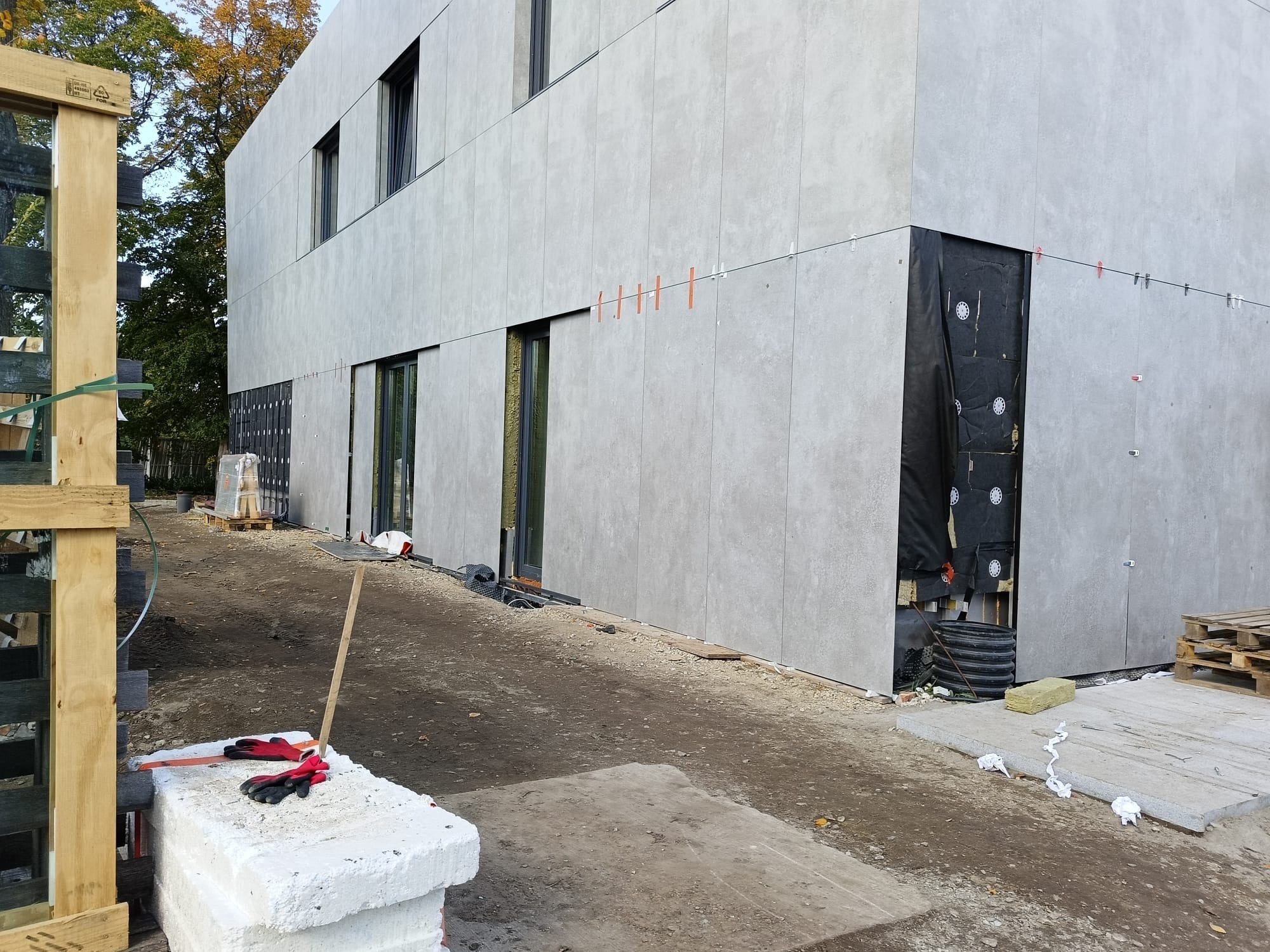 Montaż elewacji wentylowanej z płyt włókno-cementowych na dwukondygnacyjnym budynku. Widoczne detale mocowania i izolacja. Częściowo ukończona fasada.