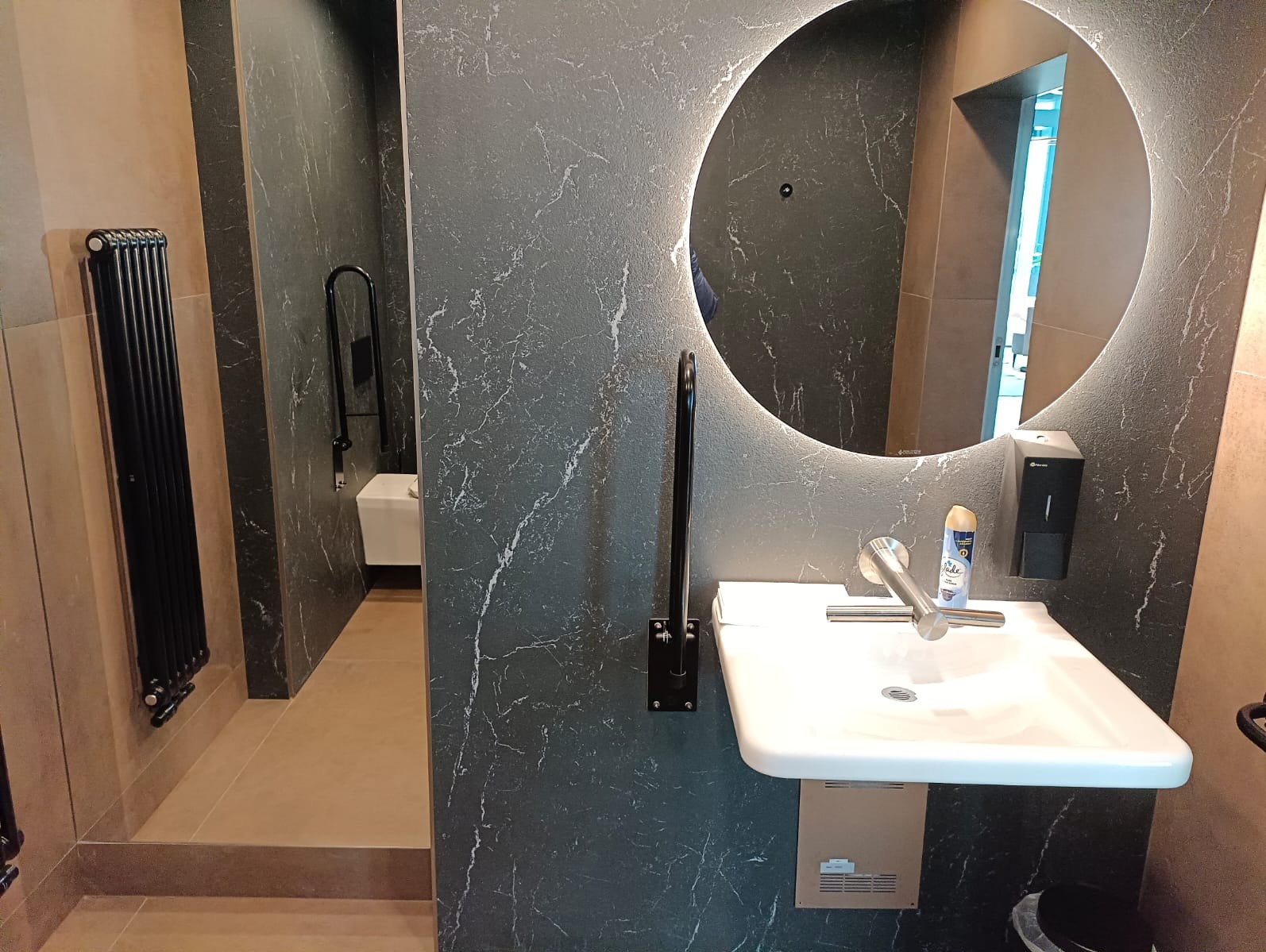 Nowoczesna łazienka w Pruszowicach z umywalką, okrągłym lustrem z podświetleniem LED i czarnymi akcentami na ścianach imitujących marmur.