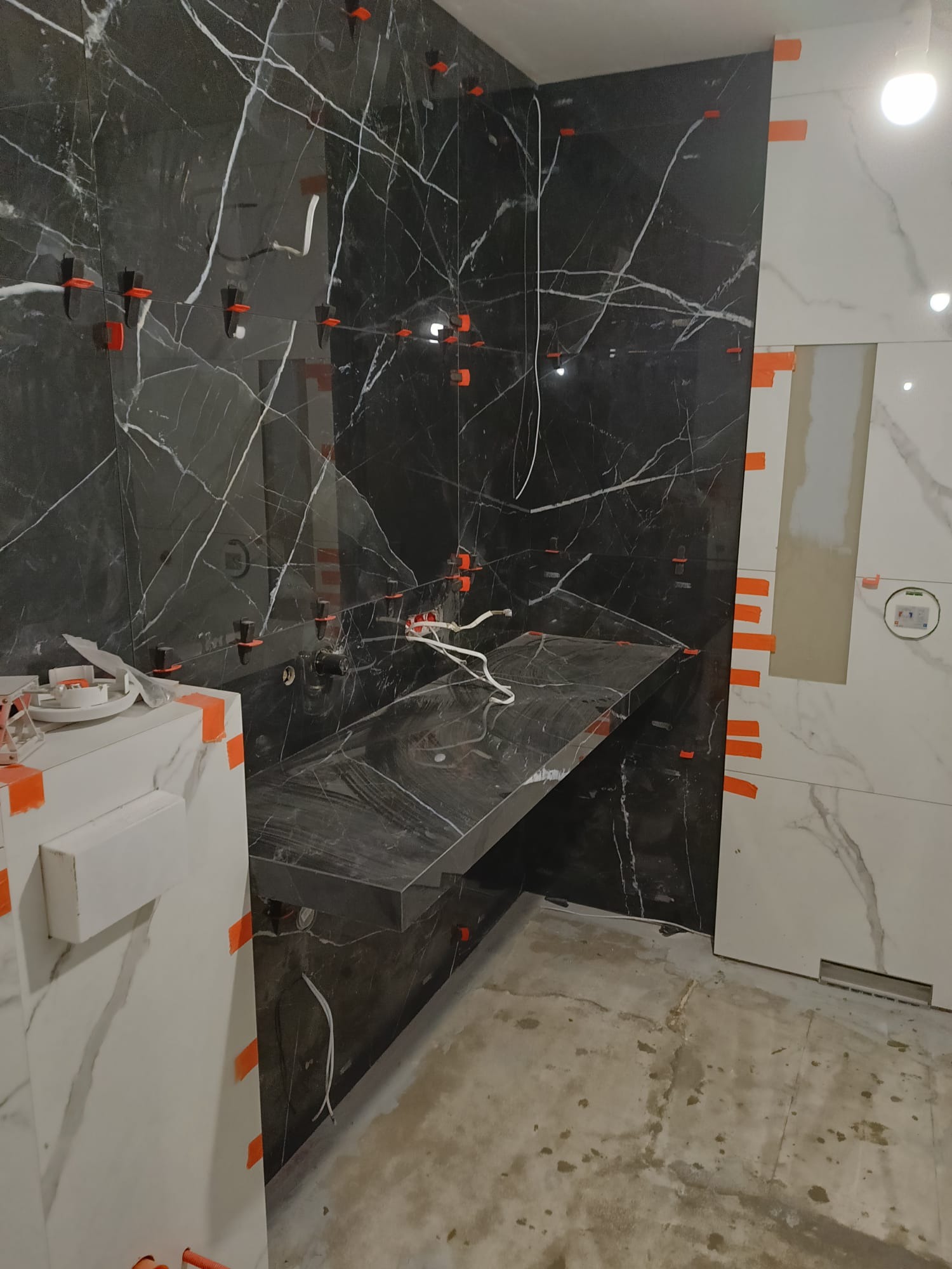 Montaż czarnych i białych płytek marmurowych w łazience, z użyciem klipsów poziomujących. Widoczny fragment blatu i instalacja pod umywalkę.