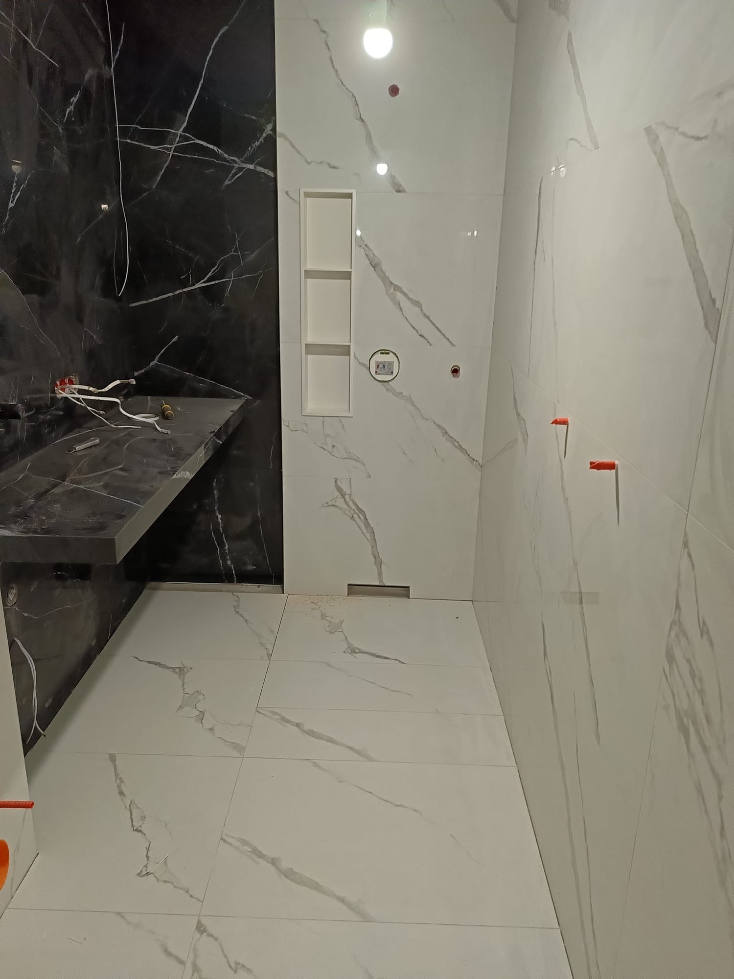 Nowoczesna łazienka w trakcie wykańczania: białe i czarne płytki imitujące marmur, widoczne narzędzia glazurnicze, półki wnękowe. Minimalistyczny design.