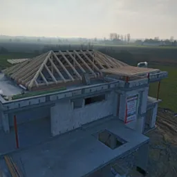 Budowa domu w trakcie: wzniesione ściany z betonu komórkowego, częściowo wykonana drewniana konstrukcja dachu. Widok z góry na budynek i okolicę.