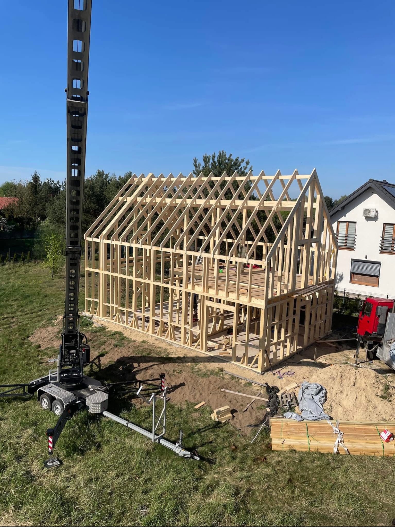 Konstrukcja domu w trakcie budowy, drewniana więźba dachowa, dźwig budowlany w tle, błękitne niebo. Widok z góry.