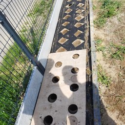 Usługi pielęgnacji ogrodów - Przygotowany teren pod trawnik z rolki. Widoczna mata z wyciętymi otworami i szablon z otworami na sadzonki. Ogrodzenie panelowe w tle.