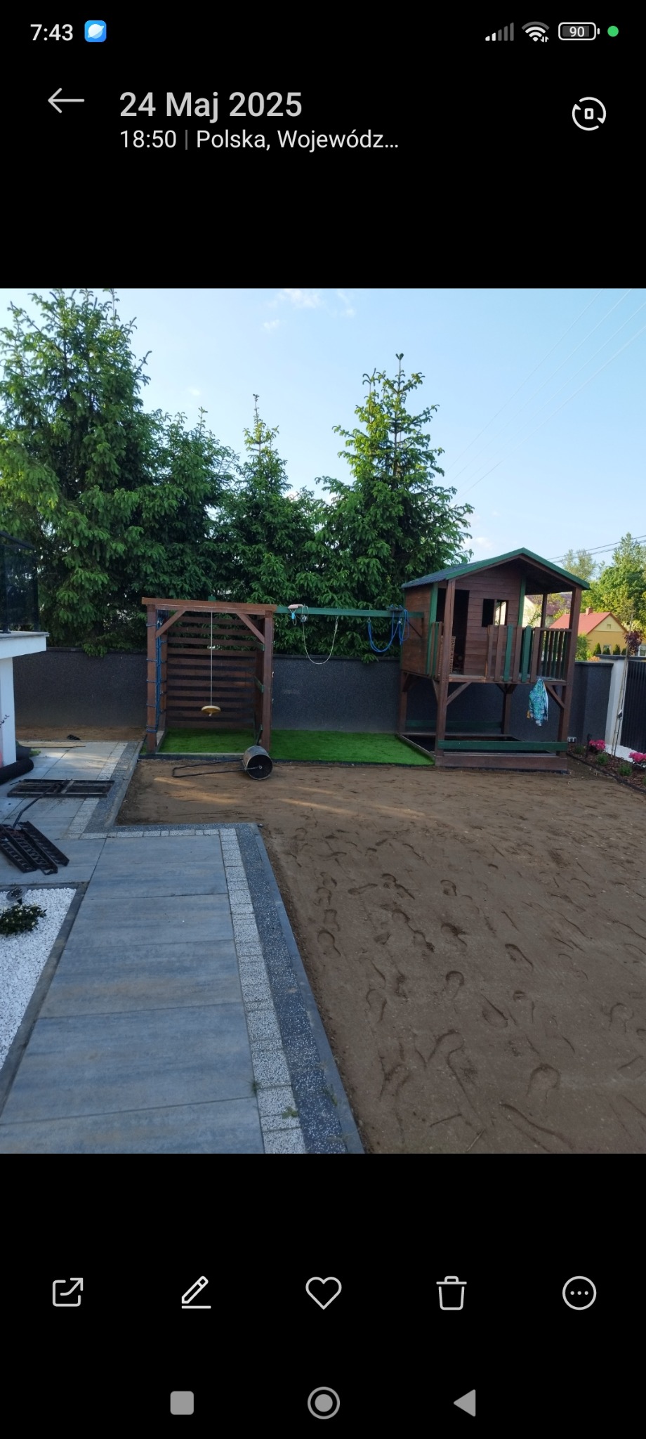 Nowoczesny plac zabaw z domkiem i huśtawką, trawa z rolki, świeżo ułożona kostka brukowa, przygotowany teren pod trawnik. Widoczne ślady stóp na ziemi.