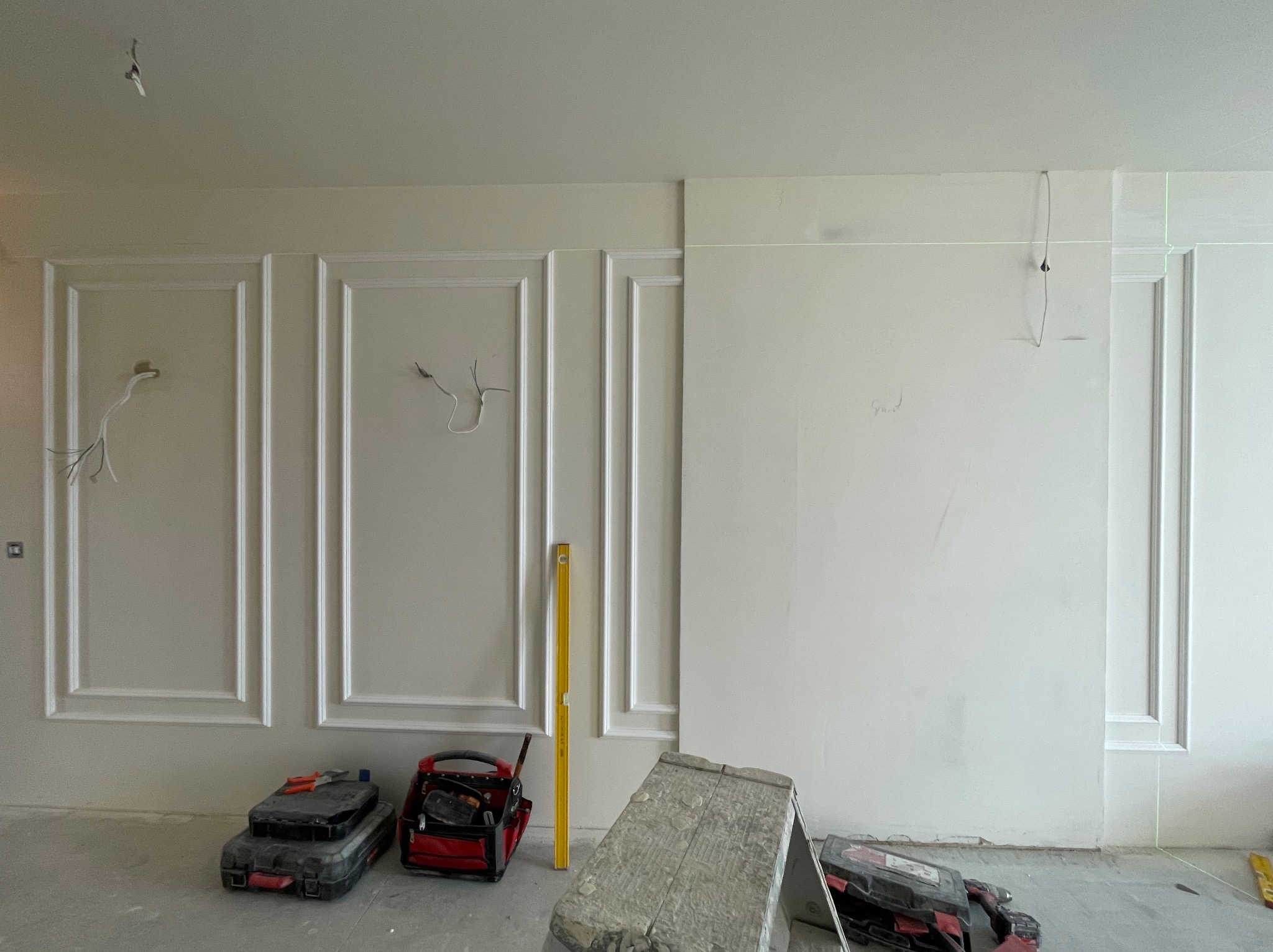 Wnętrze w trakcie prac wykończeniowych: zamontowane listwy dekoracyjne na ścianie, narzędzia pracy, poziomica. Widoczna linia lasera.