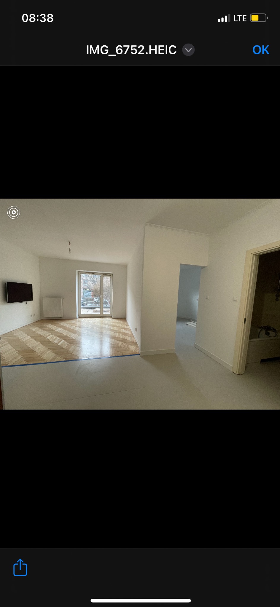 Jasne, przestronne wnętrze po remoncie: parkiet w jodełkę zabezpieczony taśmą, świeżo pomalowane ściany, widok na balkon i wyremontowaną łazienkę.