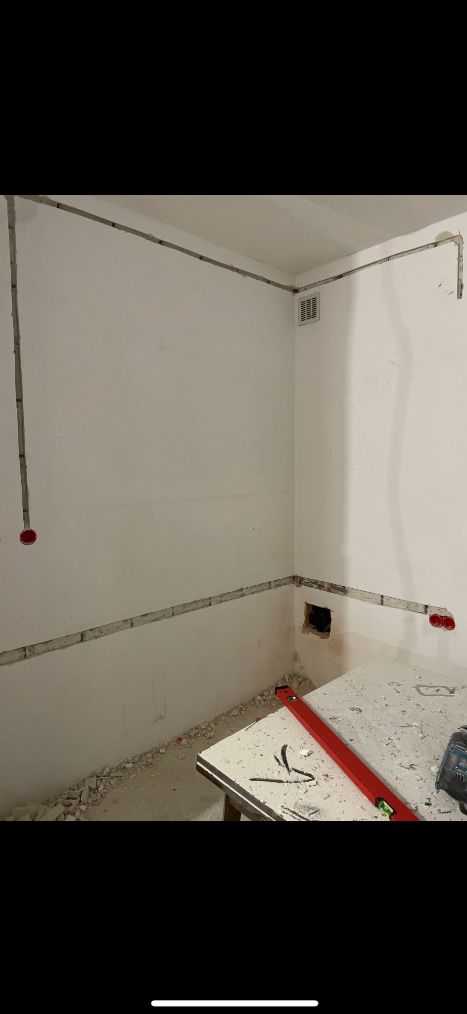 Bruzdy pod instalację elektryczną w ścianie, widoczne puszki. Na stole poziomica i narzędzia. Przygotowanie do wykończenia wnętrza.