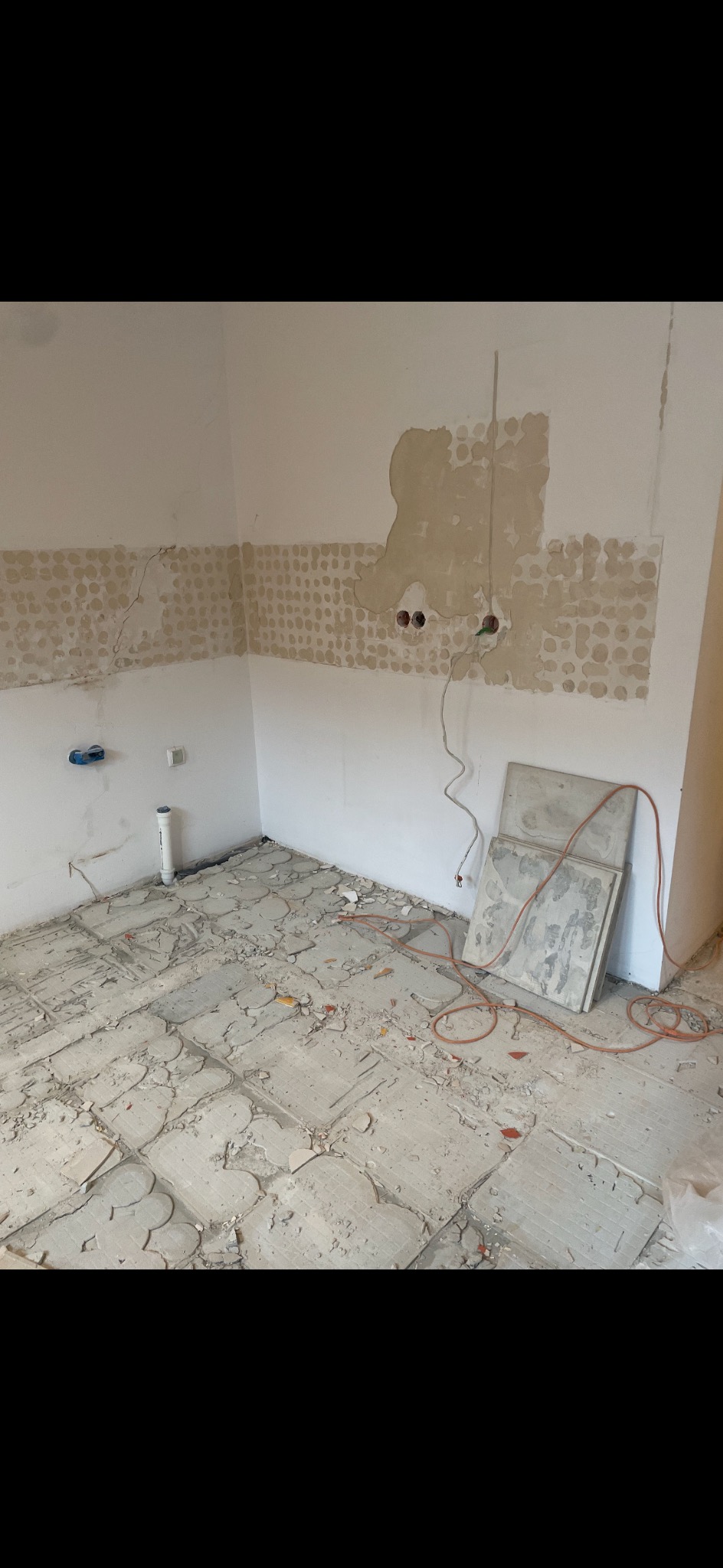 Demontaż płytek w łazience. Widoczne resztki kleju i stare płytki na podłodze. Ściany częściowo przygotowane do dalszych prac.