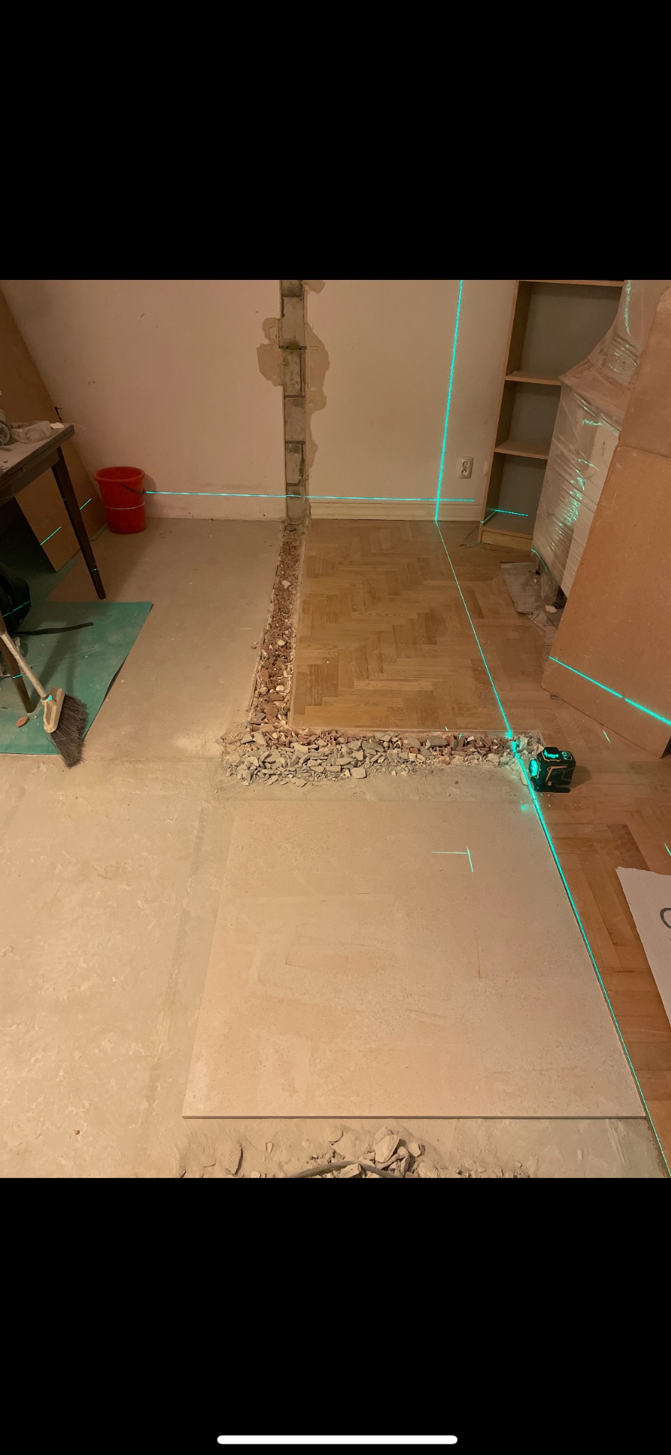 Demontaż podłogi w pokoju z widoczną warstwą betonu i fragmentem parkietu. Laserowy niwelator wyznacza poziom. Ściana z odsłoniętą cegłą.