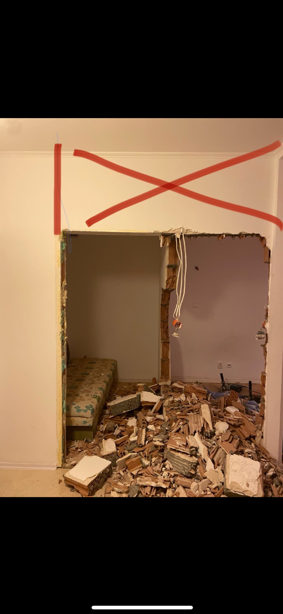 Demontaż ściany działowej z zaznaczonym obszarem do usunięcia czerwoną farbą. W tle widoczne pozostałości po rozbiórce i fragment materaca.