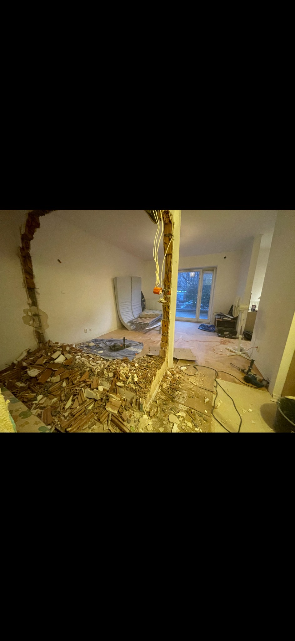 Demontaż ściany działowej w mieszkaniu: gruz, odsłonięte przewody elektryczne, widoczne narzędzia budowlane. Etap prac remontowych.