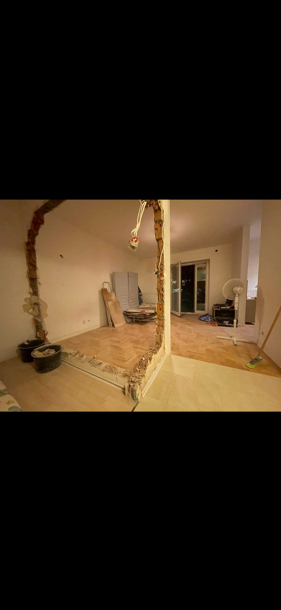 Demontaż ściany działowej z widocznymi instalacjami elektrycznymi, przygotowanie do remontu, parkiet w jodełkę, wiadro z gruzem, widok na balkon.