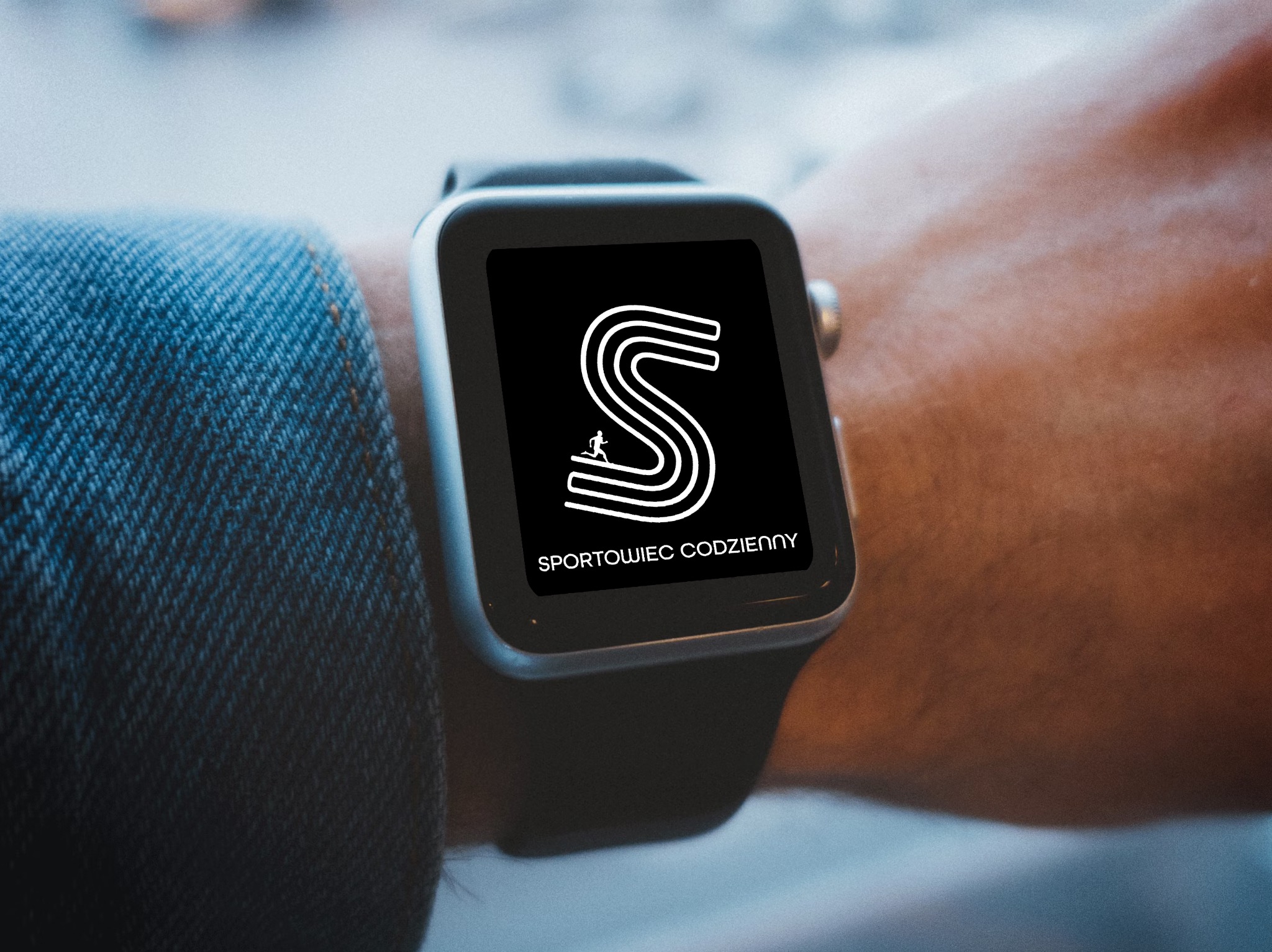 Smartwatch na nadgarstku prezentuje logo 'Sportowiec Codzienny' w formie stylizowanej litery S z biegnącą postacią, na czarnym tle.