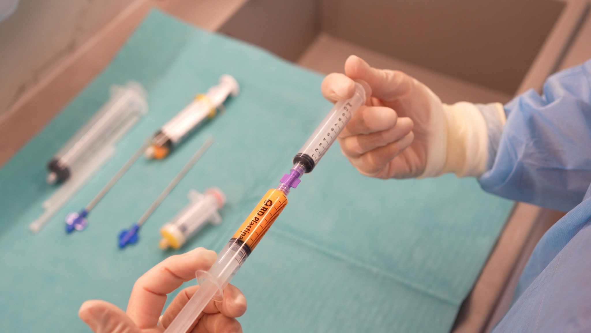 Przygotowanie do iniekcji komórek macierzystych: strzykawka z pomarańczowym płynem w dłoni w rękawiczce, inne strzykawki i narzędzia na zielonym podkładzie.