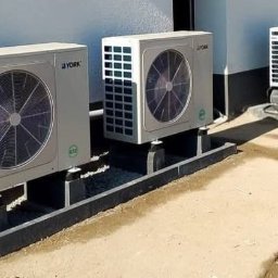 SOLAR SYSTEM Halina Karoń - Instalacja zewnętrznych jednostek klimatyzacyjnych York na betonowych podstawach, widok z boku na szare elewacje i fragment chodnika.