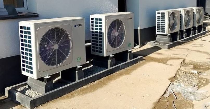 Instalacja zewnętrznych jednostek klimatyzacyjnych York na betonowych podstawach, widok z boku na szare elewacje i fragment chodnika.