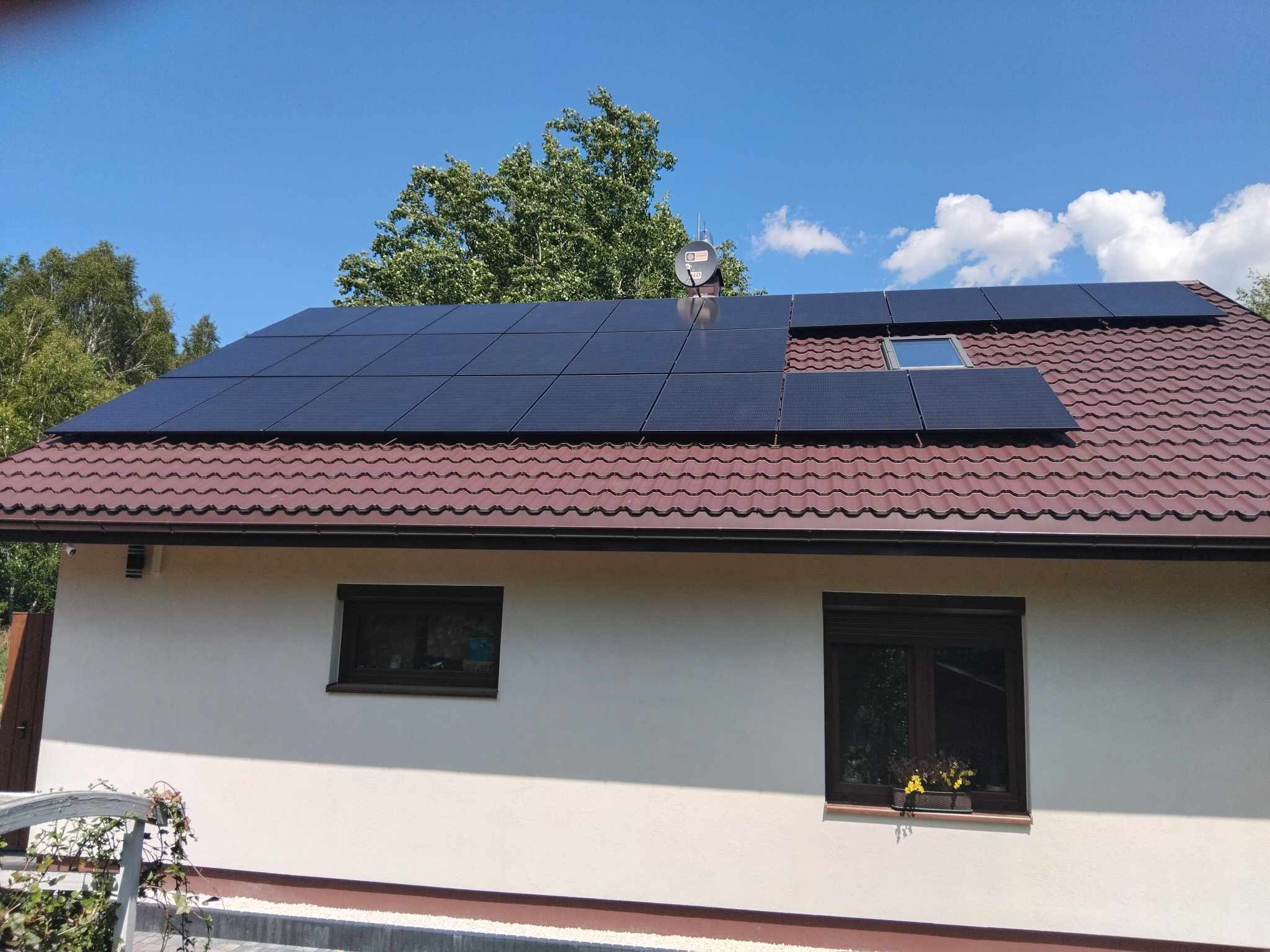 Instalacja paneli słonecznych na dachu domu z brązową dachówką i oknem dachowym, antena satelitarna na dachu, błękitne niebo.