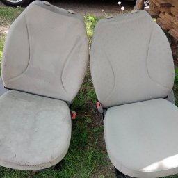 EcoClean MAŁGORZATA MIENKINA - Dwa jasne fotele samochodowe na trawie. Jeden fotel wyraźnie zabrudzony, drugi czysty, co sugeruje efekt prania tapicerki. Ujęcie z góry.