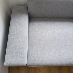 EcoClean MAŁGORZATA MIENKINA - Jasnoszara kanapa z bliska, widoczna faktura materiału, drewniana podłoga. Ujęcie z góry, delikatne światło, minimalizm.