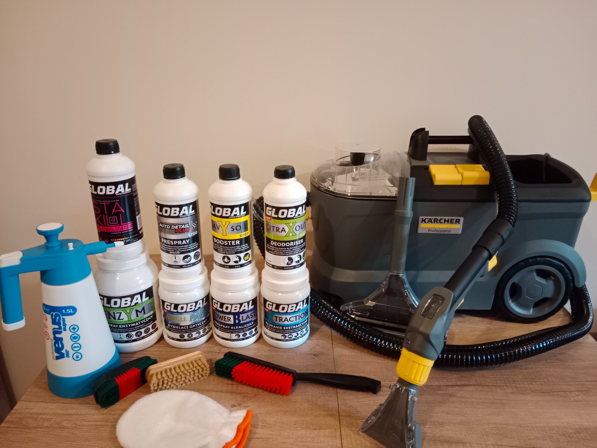 Zestaw do prania tapicerki: odkurzacz Karcher, butelki z chemią Global, spryskiwacz Venus, szczotki i ściereczka z mikrofibry na drewnianym blacie.