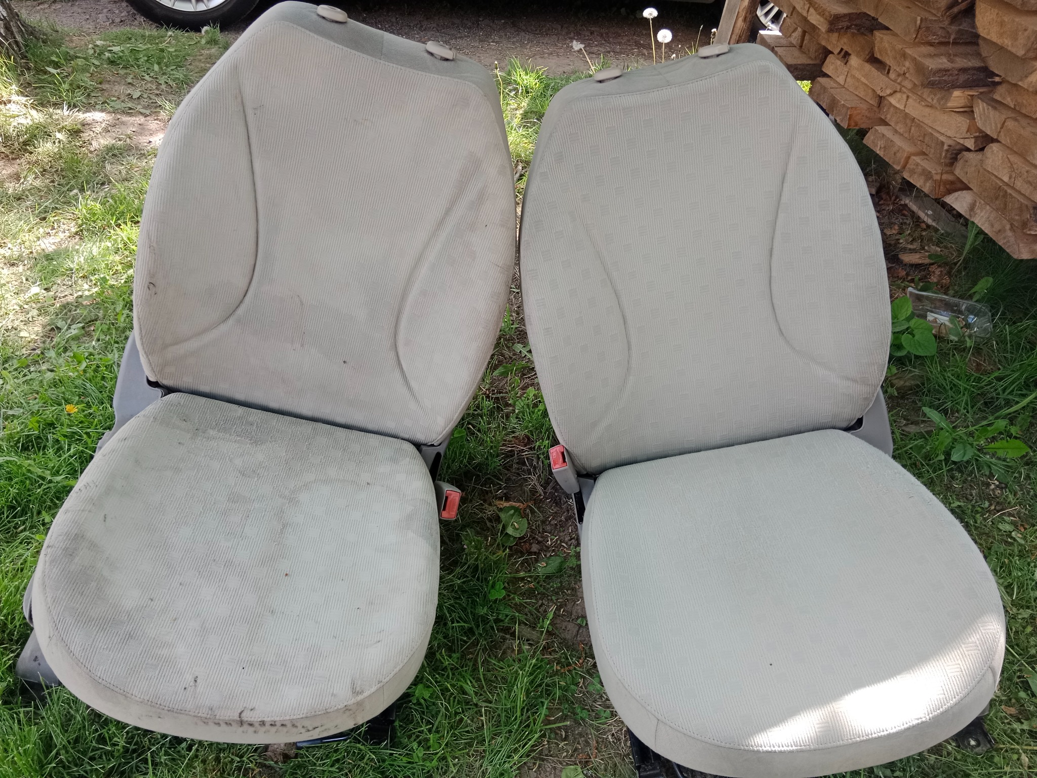 Dwa jasne fotele samochodowe na trawie. Jeden fotel wyraźnie zabrudzony, drugi czysty, co sugeruje efekt prania tapicerki. Ujęcie z góry.