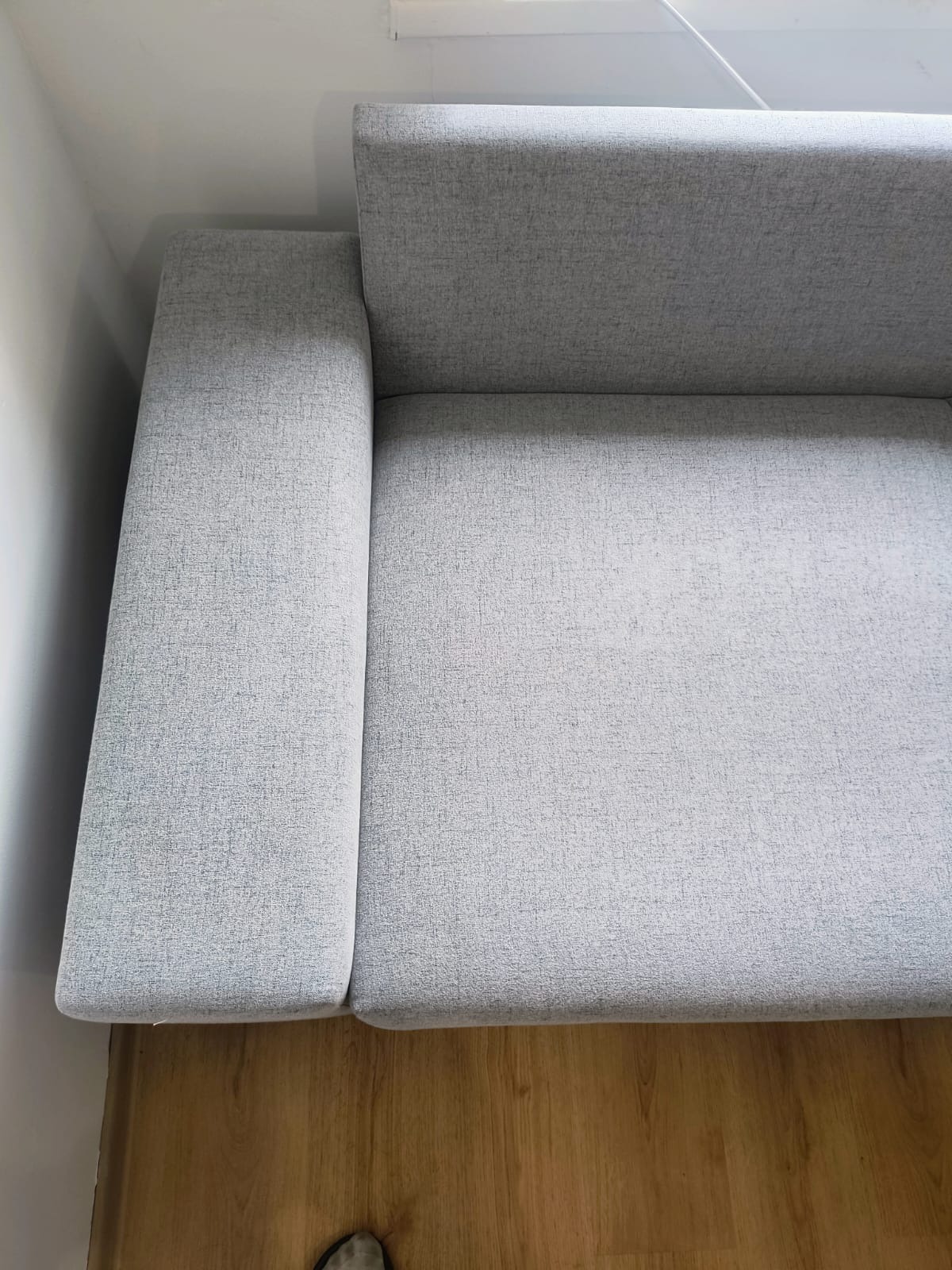 Jasnoszara kanapa z bliska, widoczna faktura materiału, drewniana podłoga. Ujęcie z góry, delikatne światło, minimalizm.