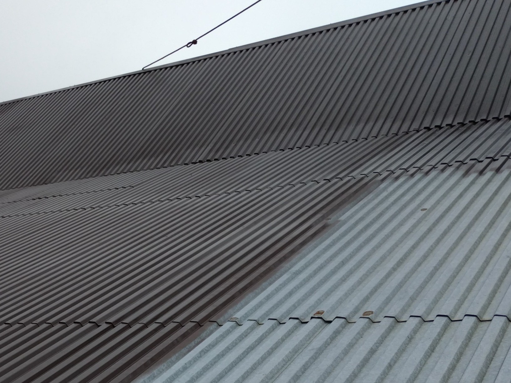 Częściowo pomalowany, blaszany dach z wyraźnym podziałem na szarą i brązową część. Widoczne złączenia blachy i linia zabezpieczająca na szczycie dachu.