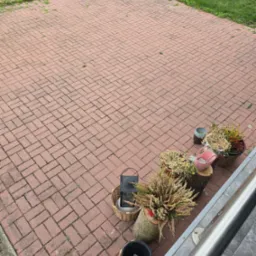 Czerwona kostka brukowa po myciu w Policach, z dekoracyjnymi roślinami w donicach i lampą ogrodową w tle. Widok z góry, czysty i zadbany teren.