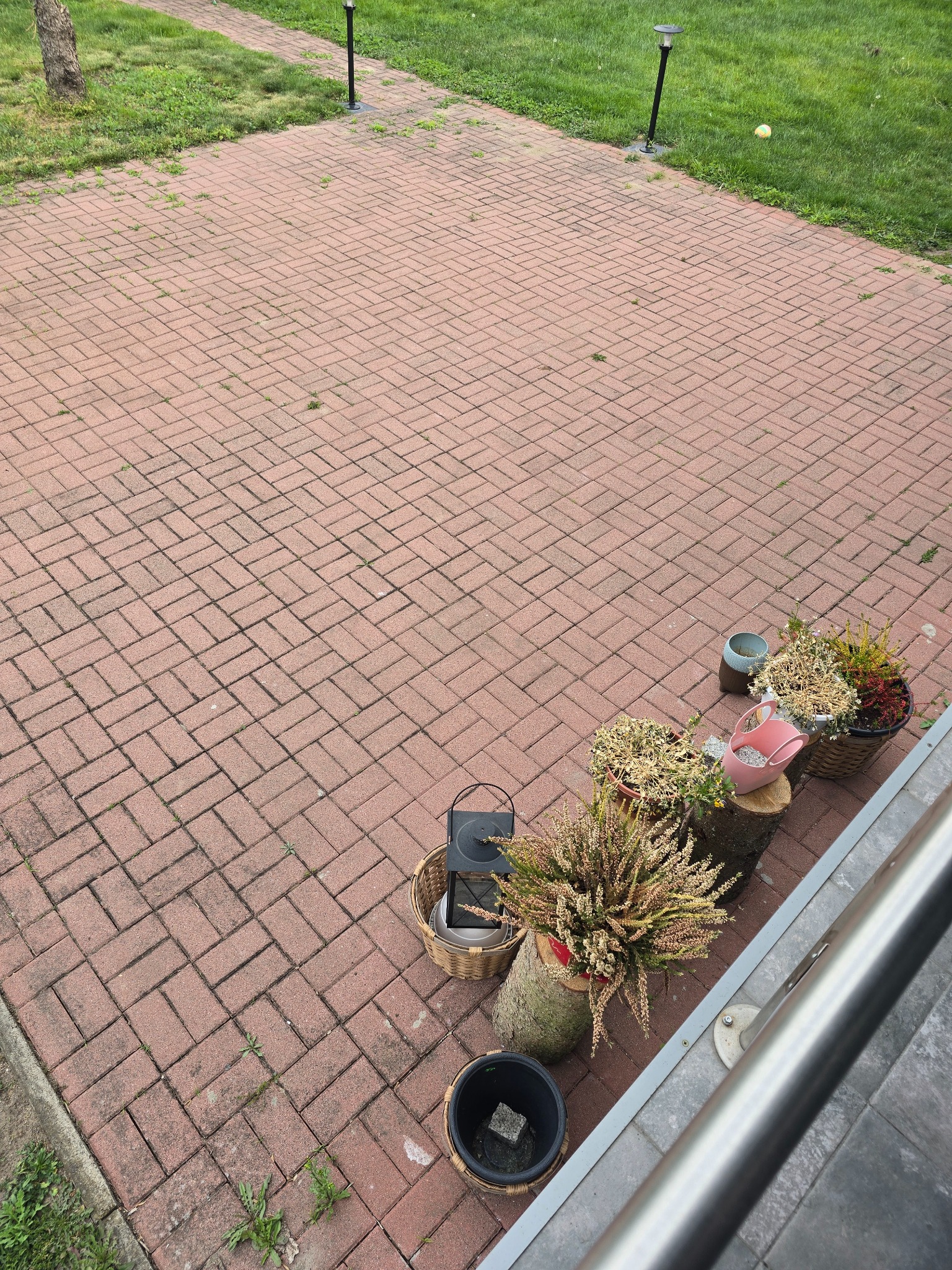 Czerwona kostka brukowa po myciu w Policach, z dekoracyjnymi roślinami w donicach i lampą ogrodową w tle. Widok z góry, czysty i zadbany teren.