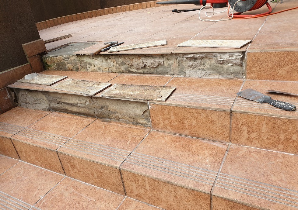 Uszkodzone schody z terakoty w Łodzi, w trakcie naprawy. Widoczne narzędzia i odspojone płytki. Prace remontowe przy zewnętrznych schodach.