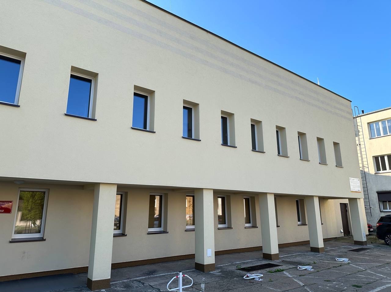 Budynek po renowacji elewacji w odcieniach beżu z rzędem okien i kolumn. Widoczne detale wykończenia i czyste linie architektoniczne. Jasne, naturalne oświetlenie.